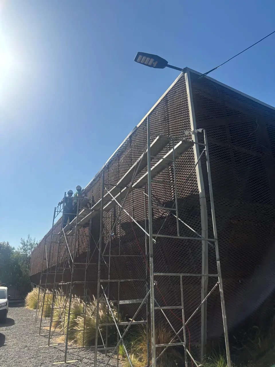 Equipo en andamio metálico trabajando en fachada con malla expansiva - Servicios Urgentes